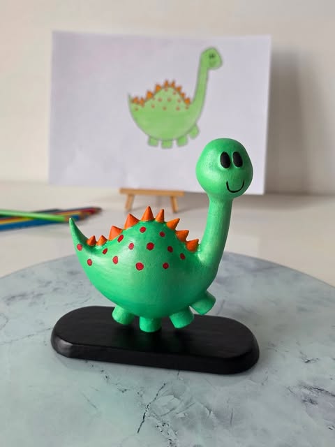 A green dinosaur art piece in front of the original child's drawing